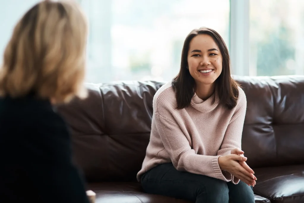 Woman in a pink sweater sitting on a brown leather couch smiling during a conversation